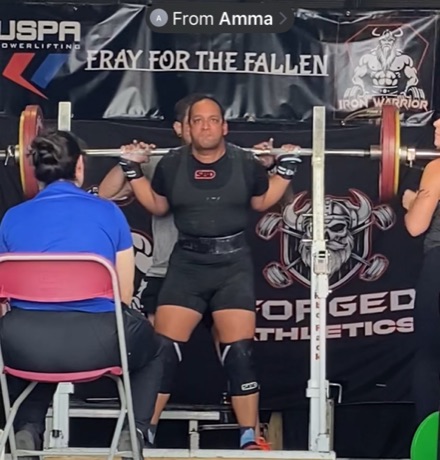 Narayana under a loaded bar at a USPA powerlifting meet, mid-squat